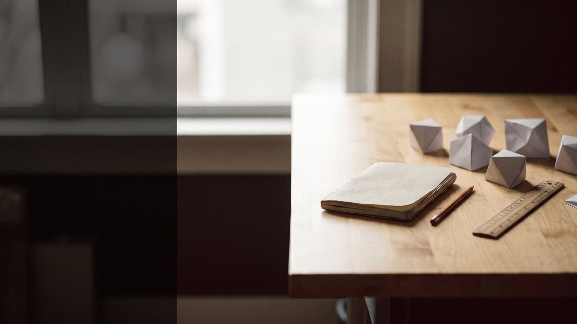 A desk with a notebook, ruler and folded paper prototypes arranged on the right third